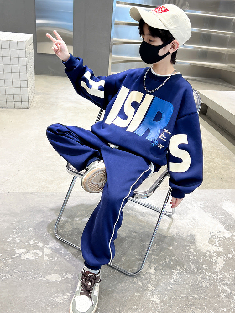 Child wearing a blue tracksuit with large white letters, sitting on a chair indoors.